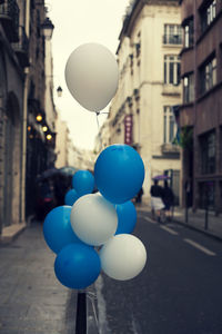 Blue and white helium balloons tied to bollard on street in city