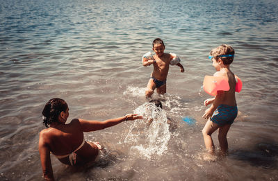 Happy boys and their mother having fun while playing in the water during summer day.