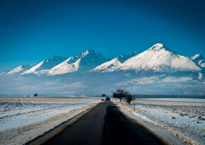 Road by snowcapped mountains against clear blue sky