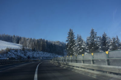 Road by trees against clear sky during winter