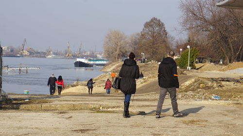 Rear view of people walking on shore against trees