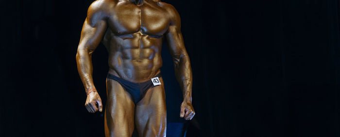 Midsection of body builder standing against black background