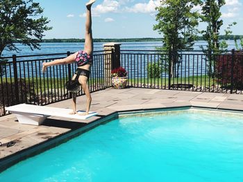 Full length of woman doing handstand at poolside against sky during sunny day