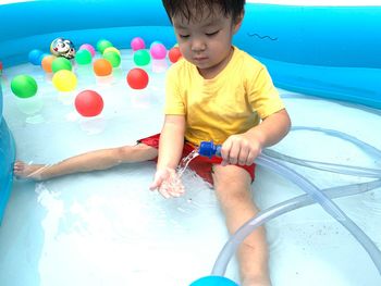 High angle view of boy holding garden hose while sitting in wadding pool