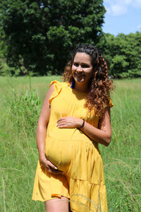 Young pregnant woman in third trimester on a day out holding her belly on green field