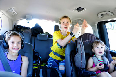 Portrait of three siblings sitting in car excited for traveling and adventures 