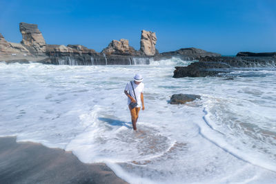 High angle view of man walking at shore against clear blue sky