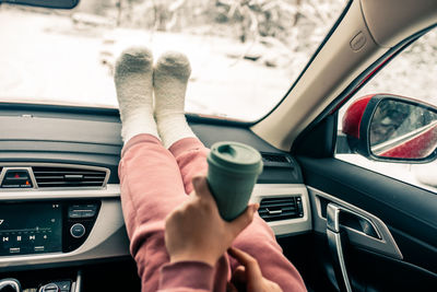 Low section of woman holding coffee cup sitting in car