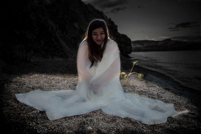 Portrait of beautiful woman wrapped in white fabric sitting on field at night