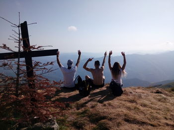 People with arms raised sitting on mountain against sky