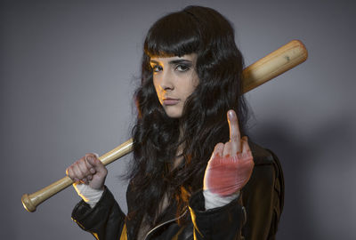 Portrait of young female model holding baseball bat against gray background