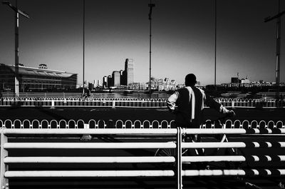 Rear view of man sitting on railing against sky