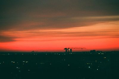 Silhouette of factory against sky at sunset