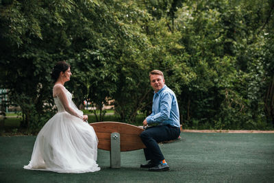 Young couple sitting on plant against trees