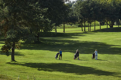 Rear view full length of women pushing golf bags on field during sunny day