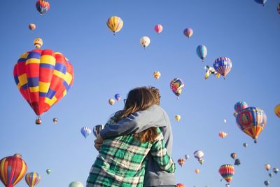 Low angle view of couple embracing against hot air balloons flying in sky
