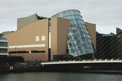 Modern buildings by river against sky in city