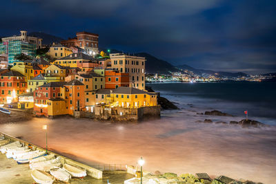 Illuminated buildings by sea against sky at night