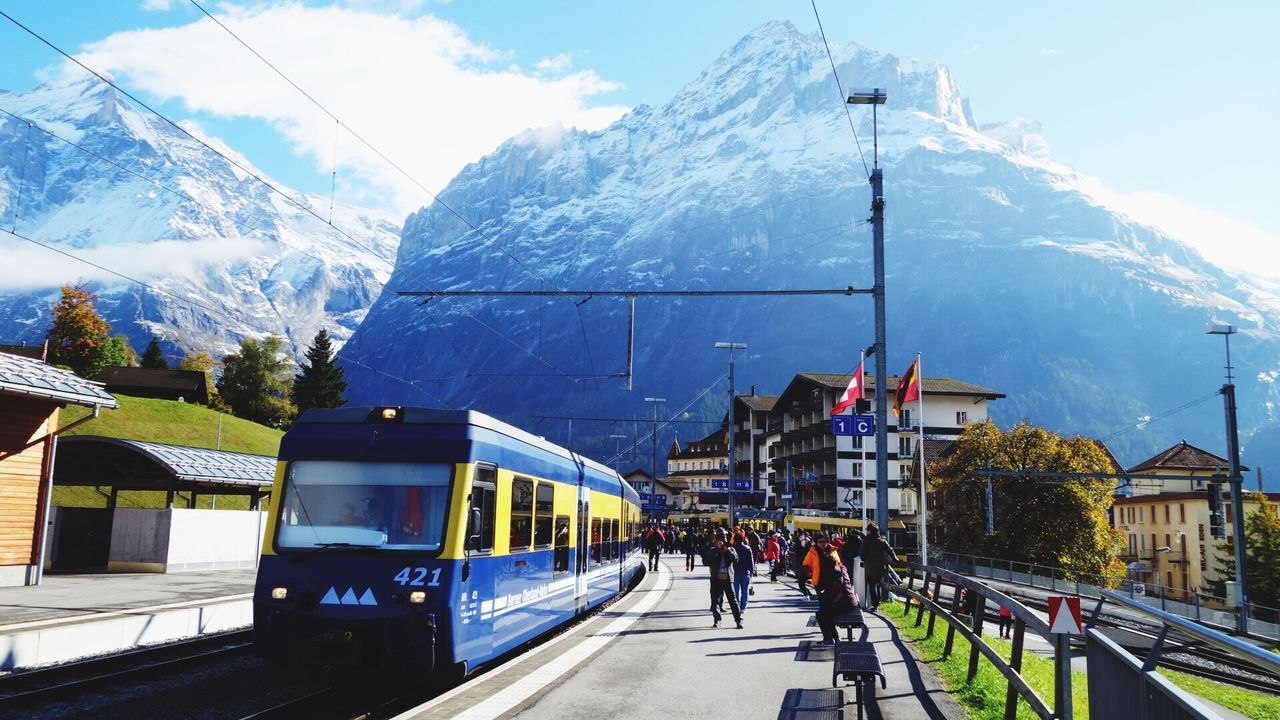 architecture, built structure, building exterior, mountain, men, transportation, mode of transport, person, cold temperature, snow, weather, winter, sky, day, blue, tourism, cloud - sky, mountain range