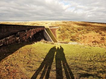 Shadow of people on grassy field against cloudy sky at avon dam