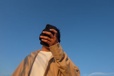 Low angle view of person photographing against blue sky