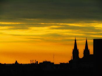 Silhouette of buildings against cloudy sky at sunset