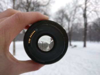 Close-up of hand holding lens in forest during winter