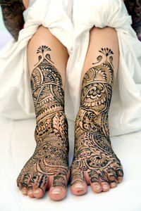 Low section of bride wearing henna tattoos on legs at home