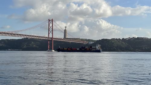 View of suspension bridge over river against cloudy sky