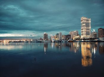 Illuminated cityscape by river against sky at night
