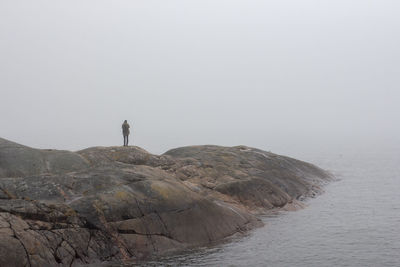 Man standing on rock by sea against sky