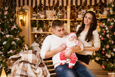 Parents celebrate new year's eve at home with small child, sitting by christmas