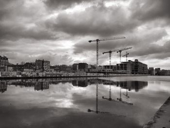 Reflection of cranes and buildings in puddle against cloudy sky at dusk