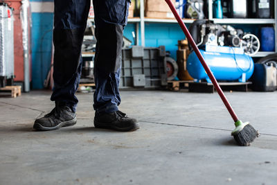 Low angle of man in uniform sweeping floor with broom while working in garage