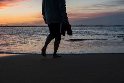 Low section of man walking on beach during sunset