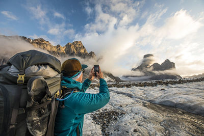 Backpacker uses smartphone to take a photo of mount asgard.