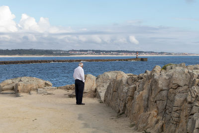 Rear view of man standing by rocks against sea