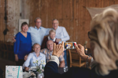 Senior woman photographing happy friends sitting at table in restaurant
