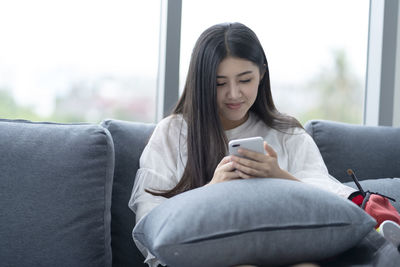 Young woman using mobile phone while siting on sofa at home