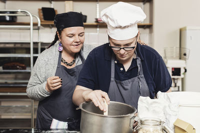 Mature baker helping coworker in cooking at commercial kitchen