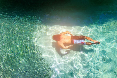 High angle view of shirtless man swimming by fish in sea