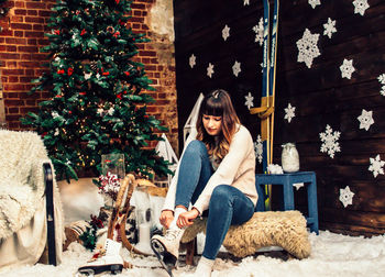 Young woman wearing shoes while sitting by christmas tree at home