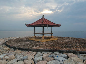 Pagoda style hut on rocks in sea against sky