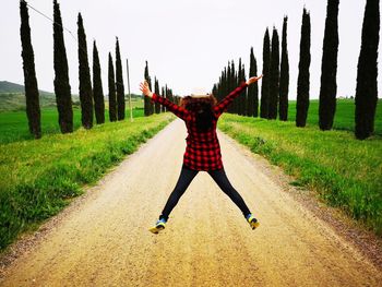 Rear view of woman jumping on dirt road