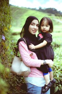 Portrait of happy mother and daughter standing against trees