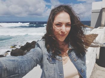 Portrait of young woman with tousled hair against sea at beach