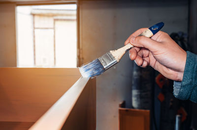 A carpenter applies lacquer paint to a wooden product with a brush