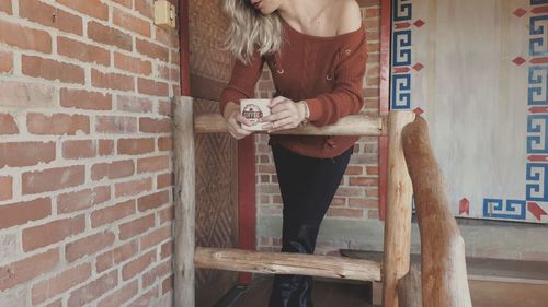 Full length of young woman standing against brick wall