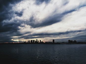 City at waterfront against cloudy sky