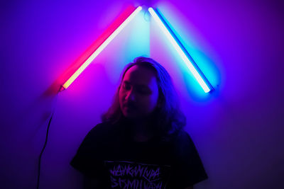 Young woman standing against illuminated wall